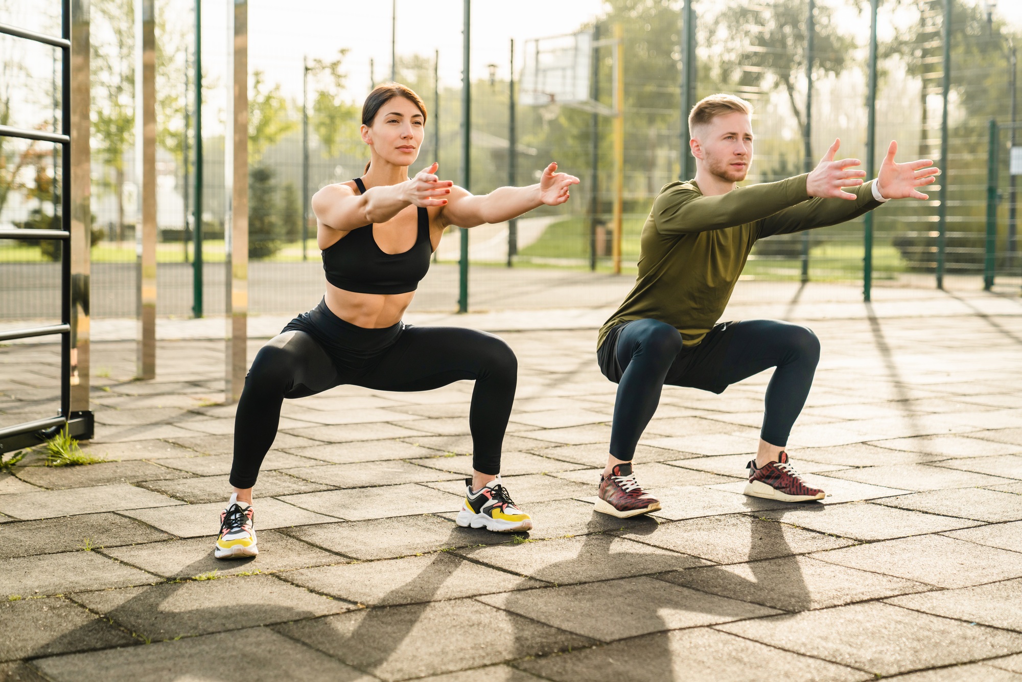 Two sporty caucasian 20s athletes doing warming-up excersises on sports ground in summer